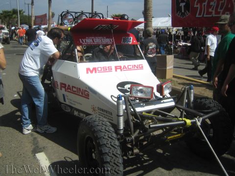 1990 Ford Bronco - white off-road race buggy lettered 'Moss Racing' and numbered 1604 sits in a street with crew and spectators around it.