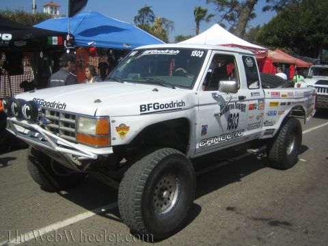 1990 Ford Bronco - white number 1503 Ford Ranger off-road race truck covered in BFGoodrich and sponsor decals, parked under canopies at an event.