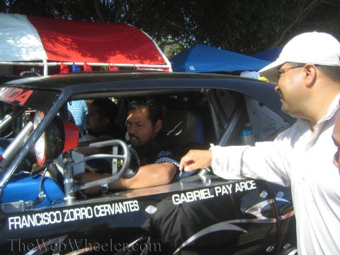 1990 Ford Bronco - seated driver in a black race truck cockpit talks with a man in white; the door reads 'Francisco Zorro Cervantes' and 'Gabriel Pay Arce'.