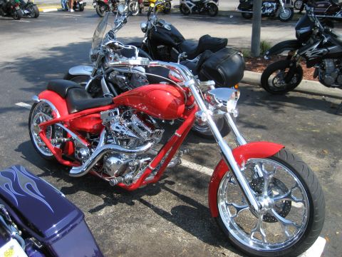 1986 Ford Bronco - A bright red custom motorcycle with extensive chrome detailing is parked outdoors, with other vehicles visible in the background.