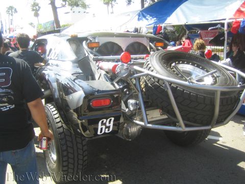 1990 Ford Bronco - Rear view of a black number 69 off-road race buggy with a tube-mounted spare tire and rear lights, parked at a busy event.