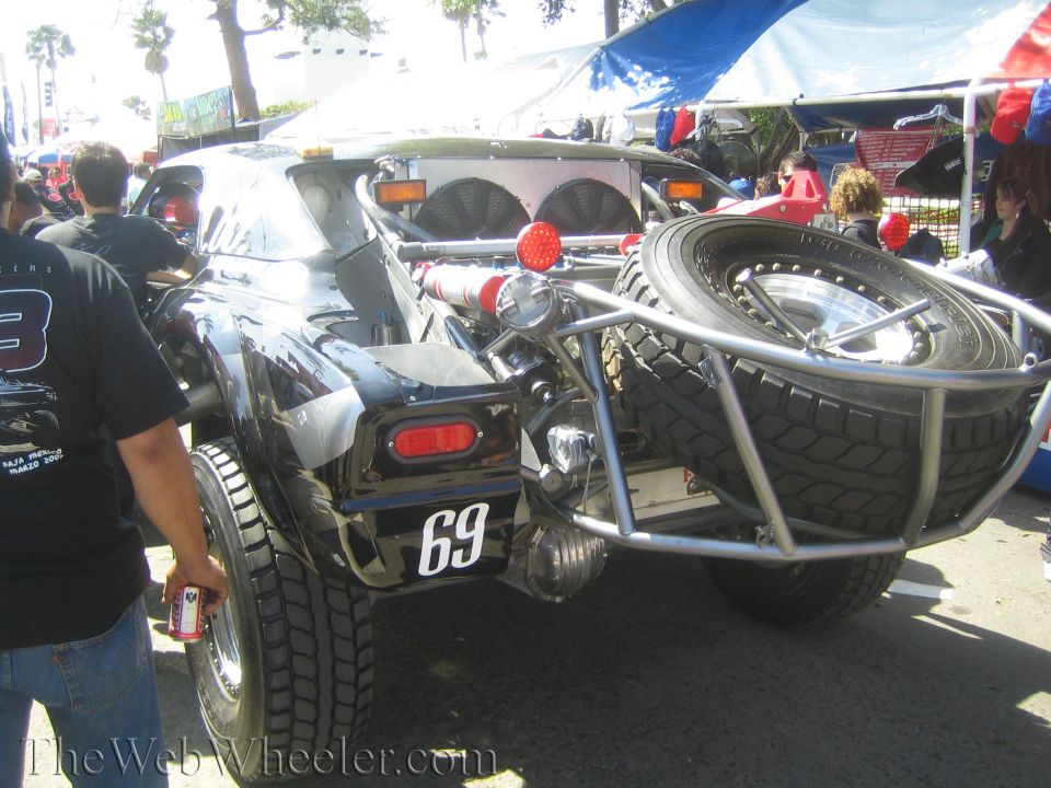 Rear view of black number 69 off-road buggy with spare tire and crowd
