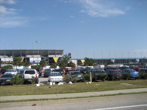 1986 Ford Bronco - A parking lot full of cars is situated in front of a large stadium under a clear blue sky.