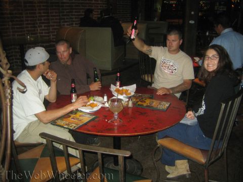 1990 Ford Bronco - Four people sit around a round red table covered with beer bottles and snacks, one man raising a bottle in a toast.