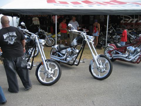 1986 Ford Bronco - Several custom choppers are on display at an outdoor event, with vendors selling apparel.