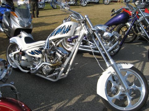 1986 Ford Bronco - A custom chopper motorcycle with unique blue flame paintwork is displayed at an outdoor event.