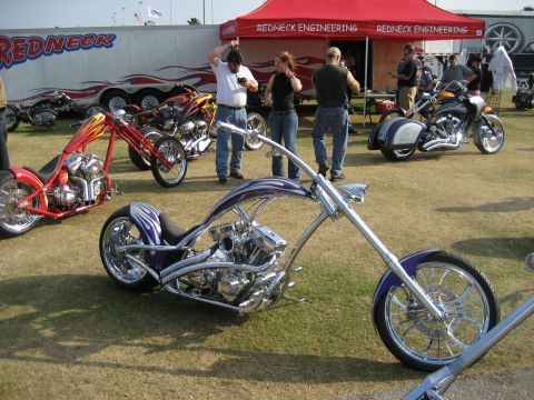 1986 Ford Bronco - Multiple custom choppers are displayed outdoors near a Redneck Engineering tent and trailer.