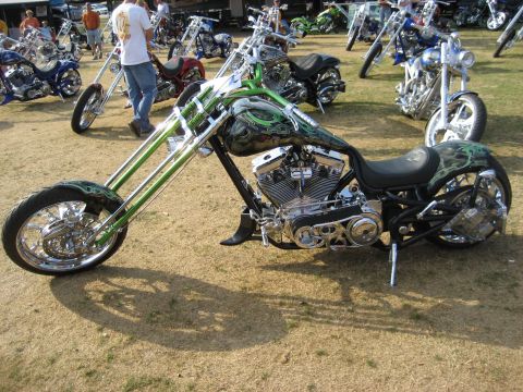 1986 Ford Bronco - A custom chopper motorcycle with intricate green flame graphics and a long, extended front fork is displayed outdoors among other motorcycl…