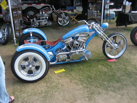 1986 Ford Bronco - A custom blue trike motorcycle with chrome accents and whitewall tires is displayed outdoors, with another motorcycle visible in the backgr…