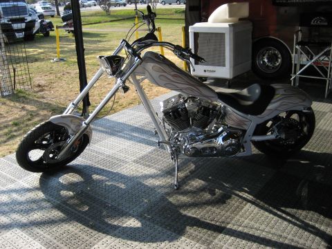 1986 Ford Bronco - A custom motorcycle with intricate flame paintwork is displayed on a patterned platform.
