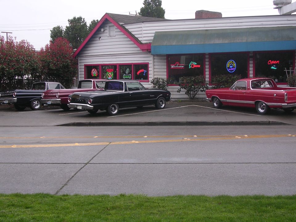 Black 1966 Ford Ranchero parked in front of a building with a red 1966 Ford Ranchero to its right