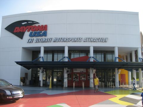 1986 Ford Bronco - The Daytona USA building, advertised as 'The Ultimate Motorsports Attraction', stands under a bright sky.