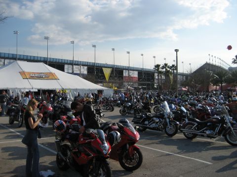 1986 Ford Bronco - A large gathering of motorcycles is parked in a lot outside a tent, with a stadium visible in the background under a partly cloudy sky.