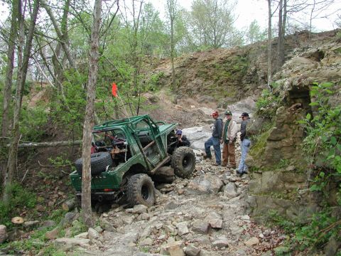 1992 Ford Bronco - A modified off-road vehicle attempts to climb a challenging rocky incline with spectators observing the action.
