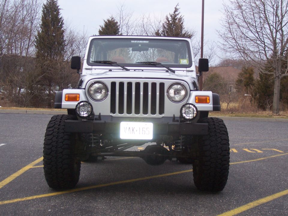 Front view of a silver Jeep Wrangler with large tires and a lift kit. License plate reads YAK-165