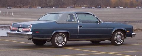 1999 Ford Crown Victoria - A blue coupe with a vinyl roof is parked in an empty lot.