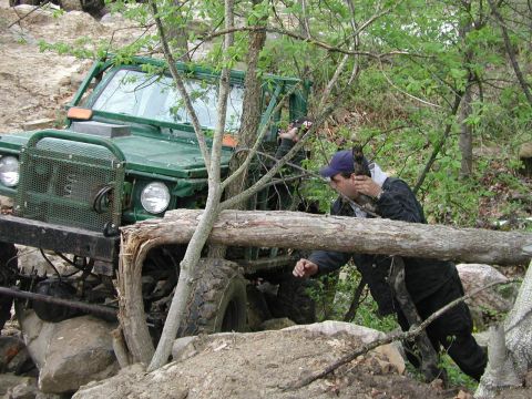 1992 Ford Bronco - A person interacts with a green off-road vehicle stuck on a rocky trail surrounded by trees.