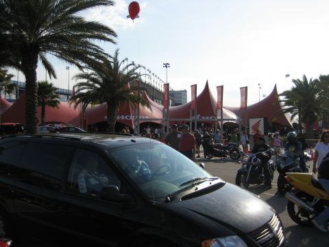 1986 Ford Bronco - A black minivan is parked in front of a large red tent structure with Honda branding, surrounded by people and motorcycles.