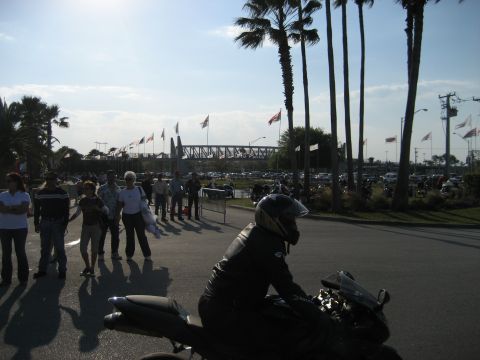 1986 Ford Bronco - A crowd gathers near a bridge, with a motorcycle rider in the foreground.