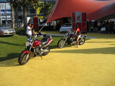 1986 Ford Bronco - Two motorcycles are displayed outdoors under a large red tent with Honda branding. A woman is seated on one of the motorcycles.