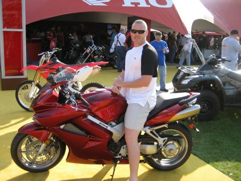 1986 Ford Bronco - Man poses with a red sport motorcycle at an outdoor event, other vehicles in background.