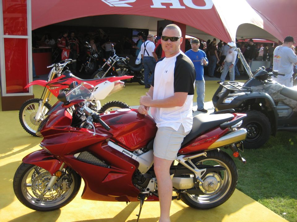 Man sits on a red sport motorcycle, with a dirt bike and ATV visible behind him