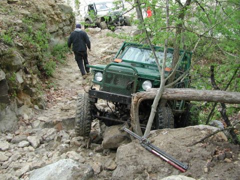 1992 Ford Bronco - A green off-road vehicle navigates a challenging rocky path, with a fallen log obstructing its front.
