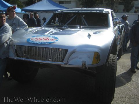 1990 Ford Bronco - Front view of a silver off-road race truck numbered 55 with a mesh grille and sponsor decals, surrounded by spectators.
