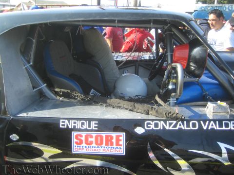 1990 Ford Bronco - Interior of a black off-road race truck with racing seats and a SCORE decal, lettered ENRIQUE and GONZALO VALDEZ on the body.