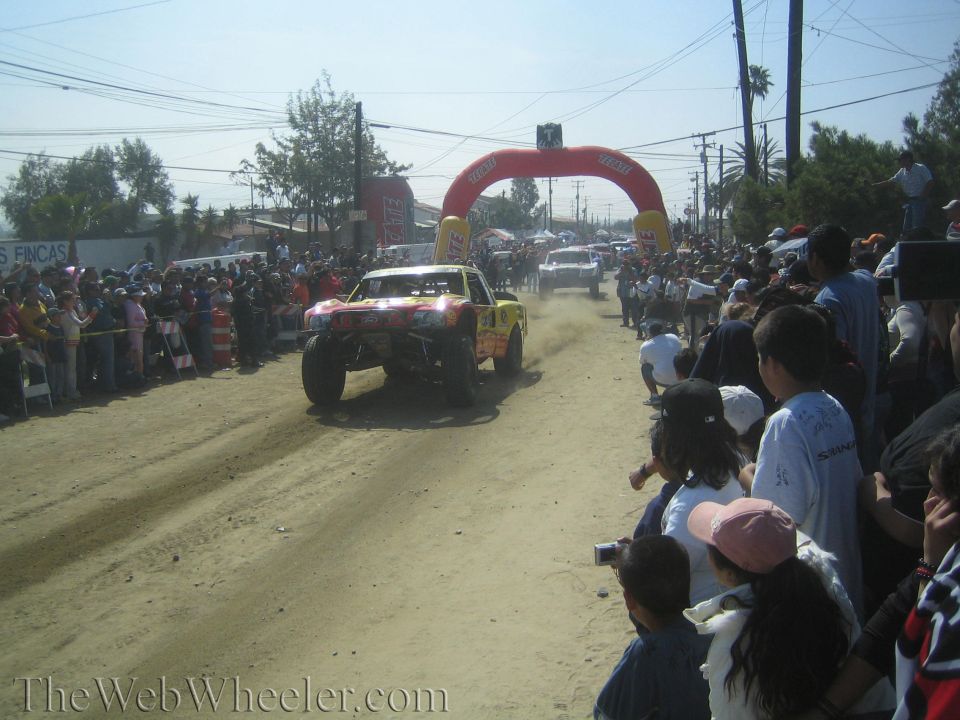 Off-road trophy truck racing down a dusty course toward inflatable arch