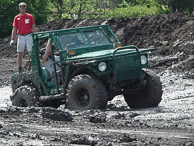 Green tube-frame buggy driving through deep gray mud at an off-road pit