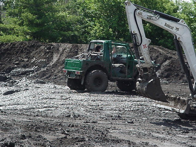 Green off-road buggy beside a white Bobcat excavator on a muddy lot