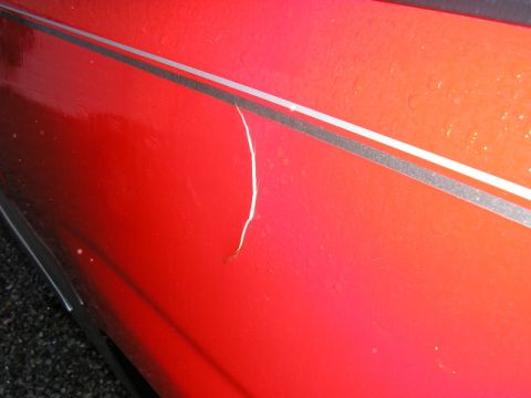 1994 Ford Probe - A crack mars the red paint on the side of a 1994 Ford Probe, which features a silver pinstripe.