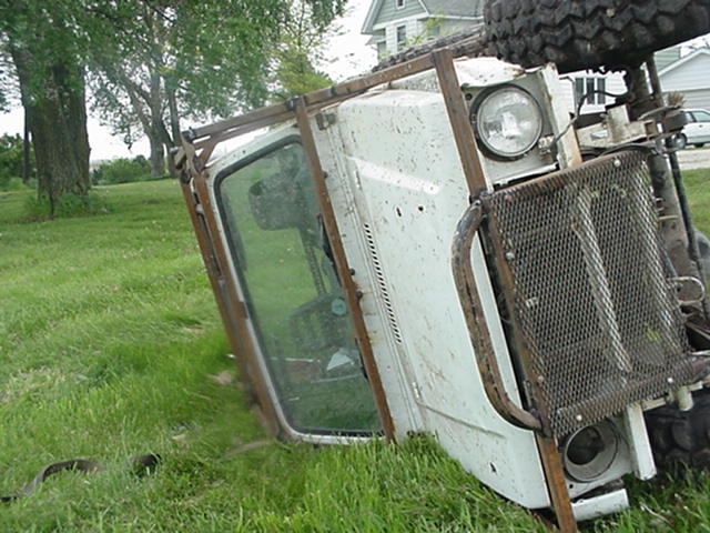 White 4x4 truck rolled onto its side near a house, showing cab and grille guard