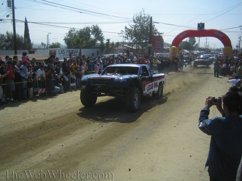 Lucas Oil sponsored off-road race truck racing on a dirt road past a large crowd