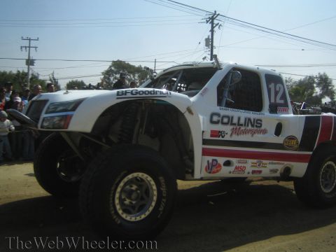 1990 Ford Bronco - white number 12 Collins Motorsports off-road race truck sits on a dirt course with BFGoodrich and sponsor decals visible.