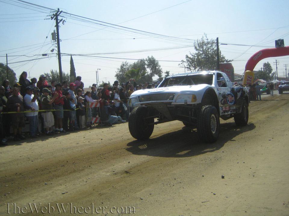 White off-road race truck airborne over a dirt course past spectators