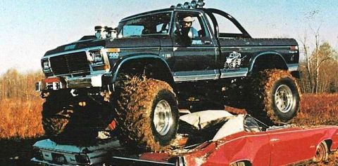 1979 Ford Bronco - A black 1979 Ford Bronco monster truck, equipped with oversized tires and a roll cage, is shown crushing a red car.