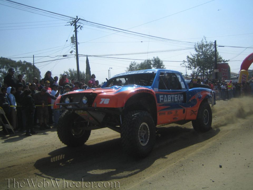 Orange and blue number 76 Fabtech off-road race truck on a dirt course