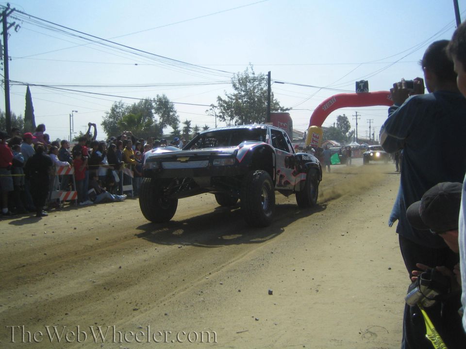 Silver and red off-road race truck on a dirt course past a crowd