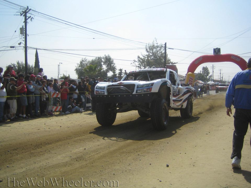 White off-road race truck racing on a dirt course past spectators