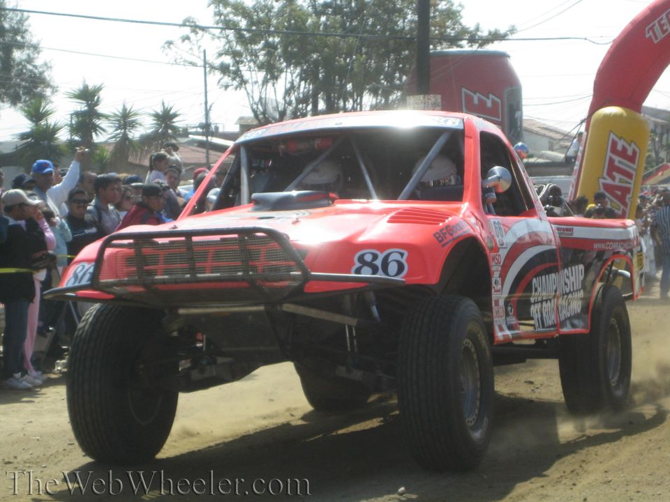 Red number 86 off-road race truck on a dirt course past a crowd