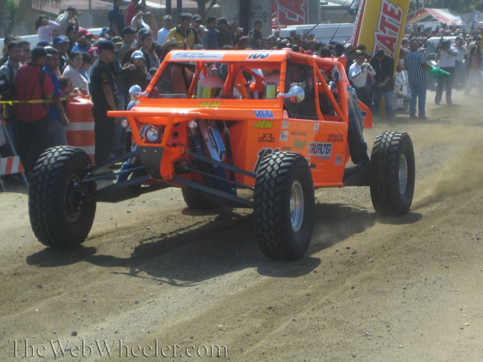 Bright orange tube-frame off-road buggy on dirt course with sponsor decals