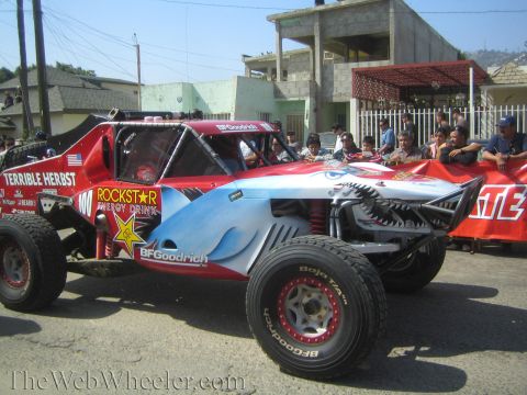 1990 Ford Bronco - red No. 100 Terrible Herbst off-road buggy with shark-mouth graphics and Rockstar Energy decals sits on a street.