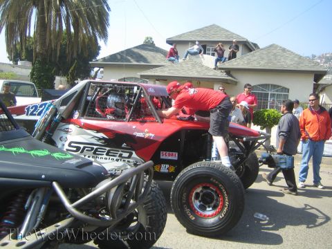 1990 Ford Bronco - Crew members work on a red Speed Technologies off-road buggy as spectators watch from a nearby rooftop.