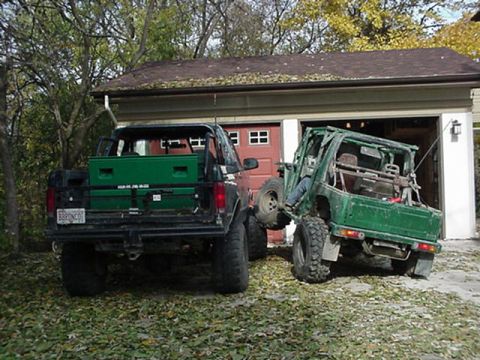 1992 Ford Bronco - Two off-road vehicles are parked in front of a garage with the doors open.