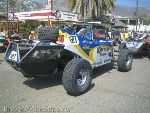 1990 Ford Bronco - Rear view of a blue and white No. 127 off-road buggy with Corona Extra decals and a mounted spare tire on a street.