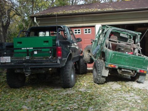 1992 Ford Bronco - Two modified off-road vehicles are parked side-by-side in front of a garage.