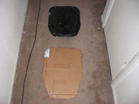 1991 Ford Bronco - A black car part and a cardboard template lie on a carpeted floor next to a doorway.