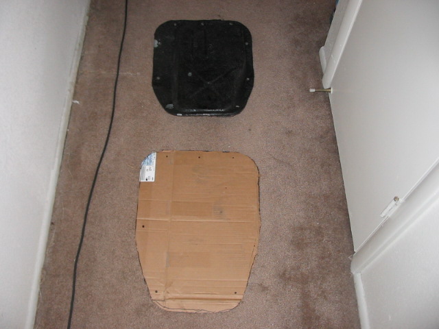 Black car part and cardboard template on brown carpet near a white door